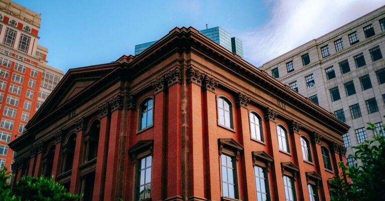A Victorian red brick building in a bustling urban cityscape with a blue sky backdrop.