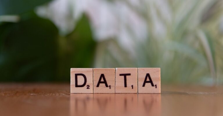 Scrabble tiles spelling 'DATA' on a wooden table with a blurred plant background.