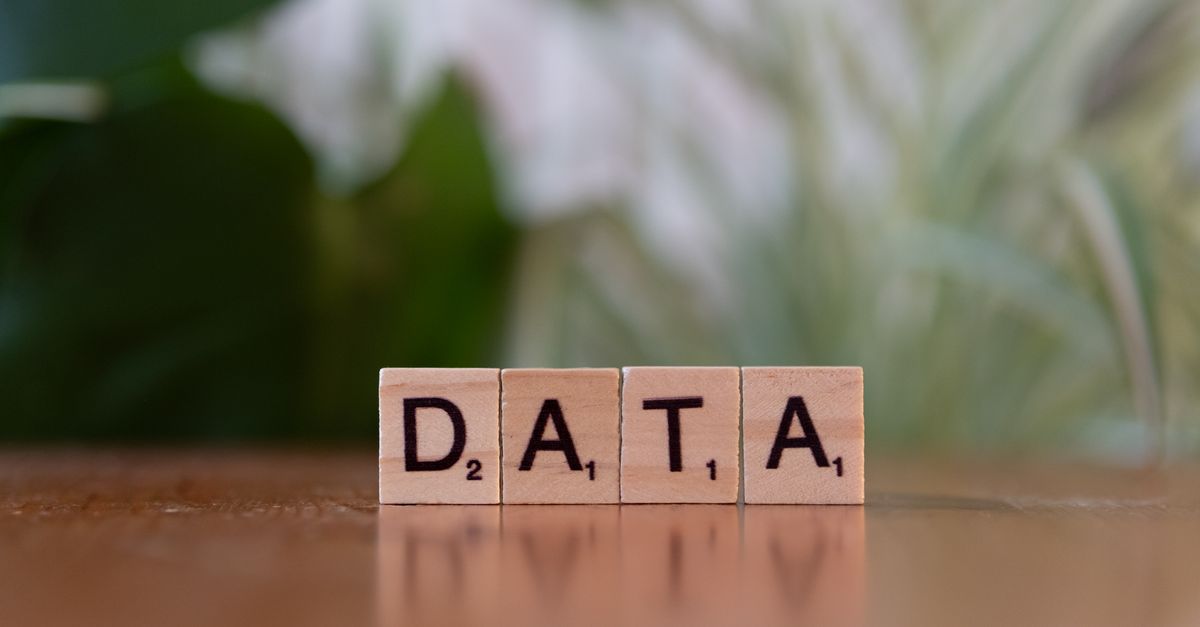 Scrabble tiles spelling 'DATA' on a wooden table with a blurred plant background.