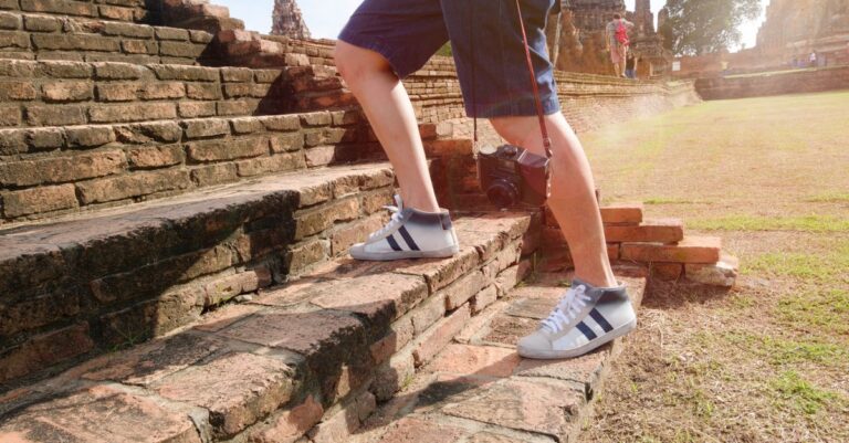 A tourist wearing sneakers climbs ancient brick steps at a historic temple site on a sunny day.