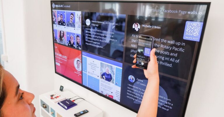 A woman uses a smartphone to scan a QR code on a digital wall display indoors.