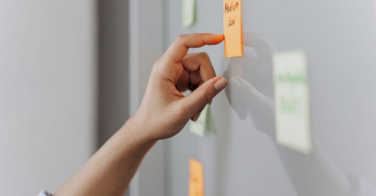 A hand placing a sticky note on a reflective surface in an office setting.