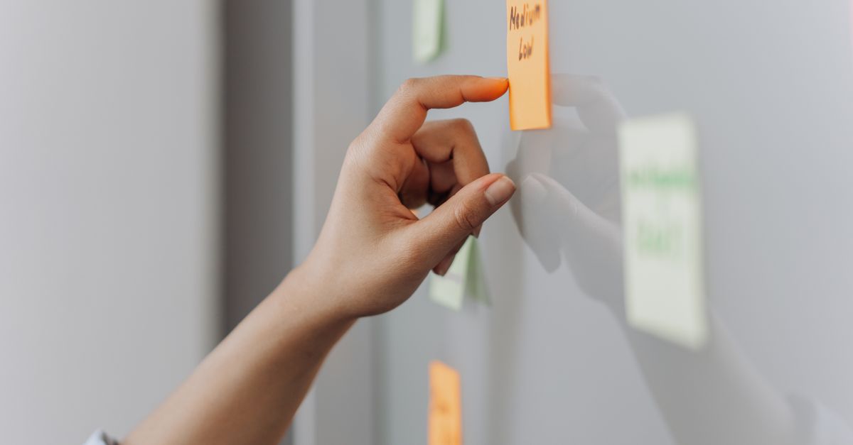 A hand placing a sticky note on a reflective surface in an office setting.