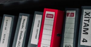 Color-coded office binders organized neatly in a storage shelf, featuring labels and a striking red binder.