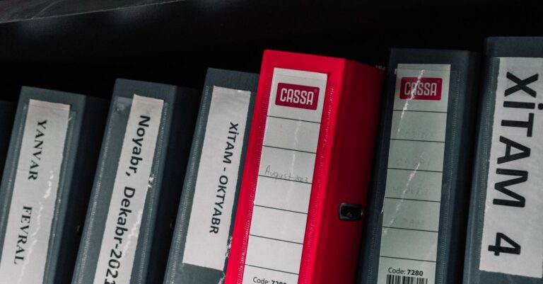 Color-coded office binders organized neatly in a storage shelf, featuring labels and a striking red binder.