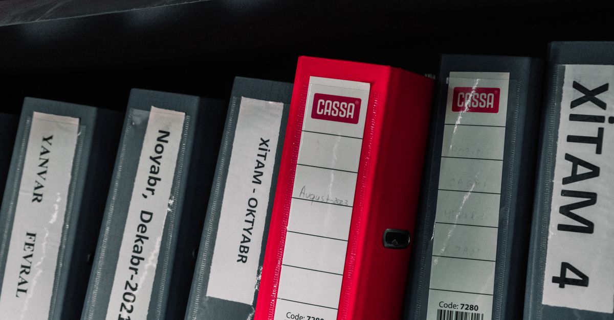 Color-coded office binders organized neatly in a storage shelf, featuring labels and a striking red binder.