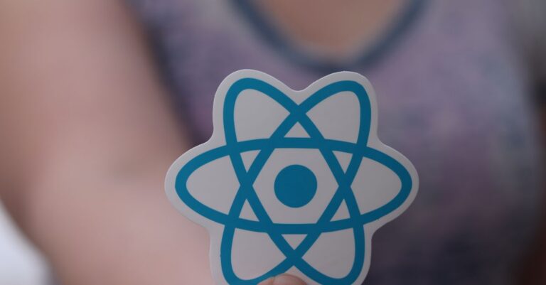 A person holds a sticker featuring the React logo, commonly used in web development.