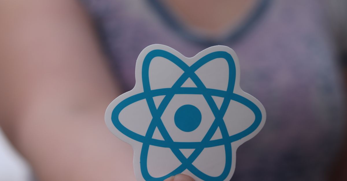 A person holds a sticker featuring the React logo, commonly used in web development.