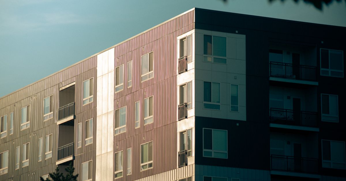 Contemporary urban apartment building with balconies and glass windows at sunset.