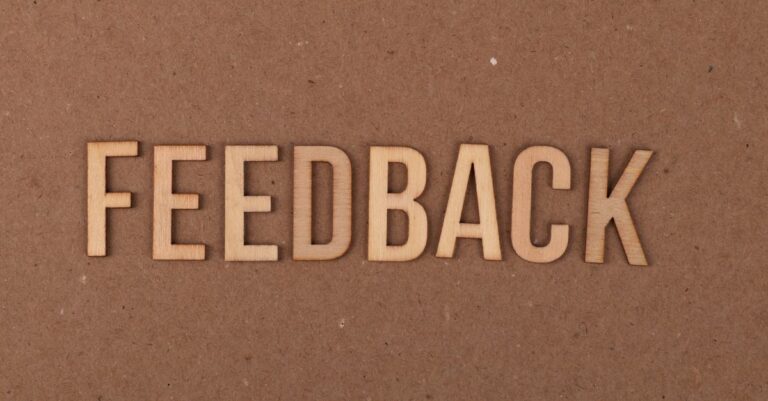 A close-up of a wooden 'FEEDBACK' sign on a textured cardboard background.