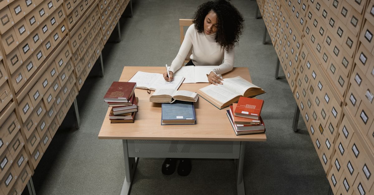 An African American woman studying at a wooden desk surrounded by drawers in an archive room.