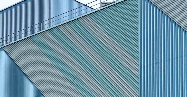 Close-up of a modern industrial building exterior with geometric metal panels and patterns.