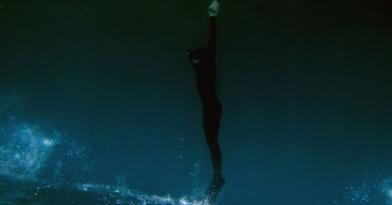 Silhouette of a diver gracefully swimming underwater in dark, deep ocean waters.