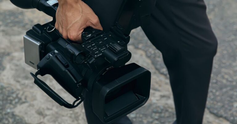 A detailed view of a person carrying a professional video camera outdoors.
