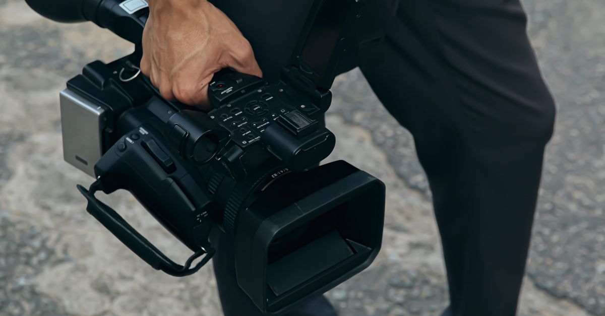 A detailed view of a person carrying a professional video camera outdoors.