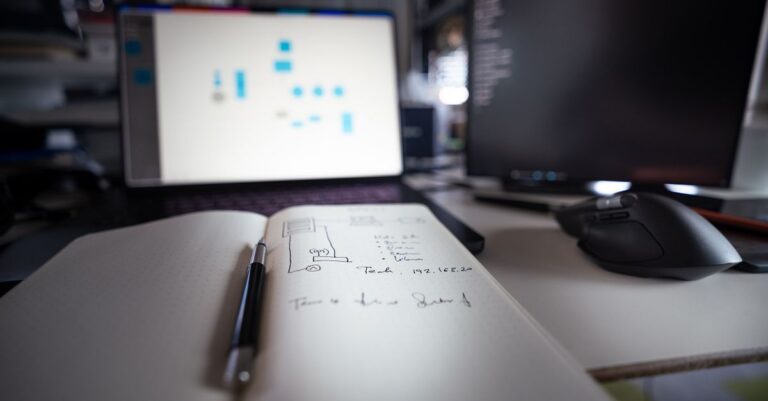 Close-up of a modern desk setup featuring notebooks, monitors, and a computer mouse.