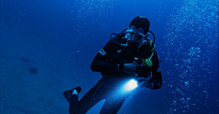 A scuba diver exploring the deep ocean with a flashlight, surrounded by bubbles and marine life.