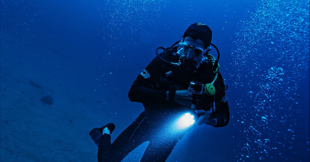 A scuba diver exploring the deep ocean with a flashlight, surrounded by bubbles and marine life.