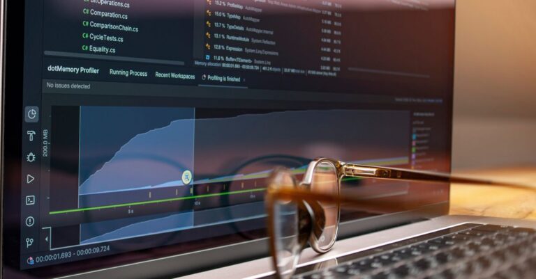 Laptop screen displaying code and performance graphs with eyeglasses resting on the keyboard.
