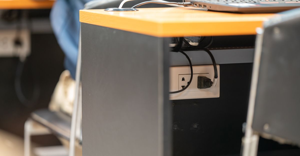 A clean office workspace featuring a desk, laptop, and hidden power cord management.