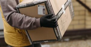 Courier holding a package marked 'TOP PACKAGING' wearing gloves for safe delivery.