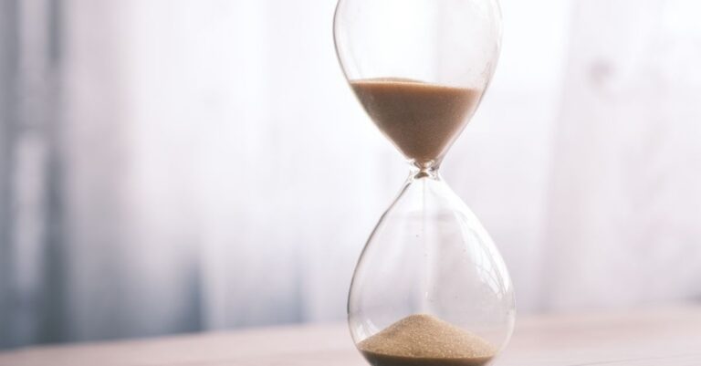 Minimalist hourglass filled with sand symbolizing time and patience, against a soft background.